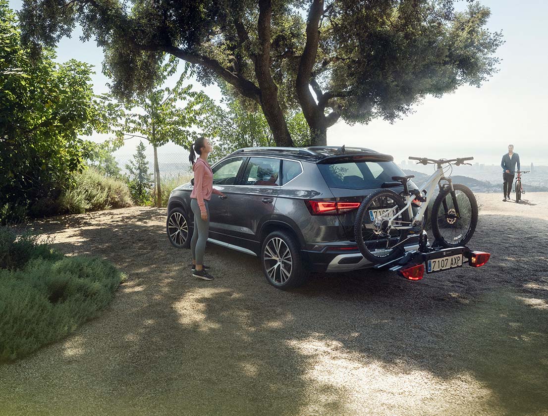 A woman standing next to a Seat Ateca with a towing bike rack accessory