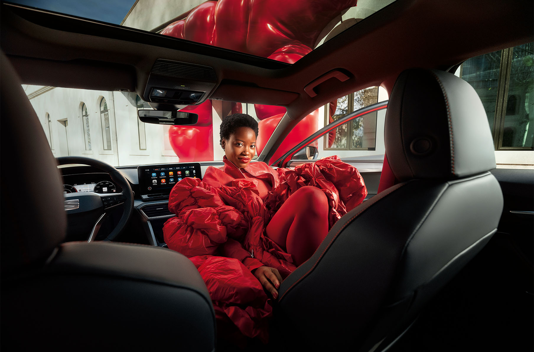 woman in red dress inside red seat leon 2024 showing dashboard, dinamica sports seats and electric sunroof